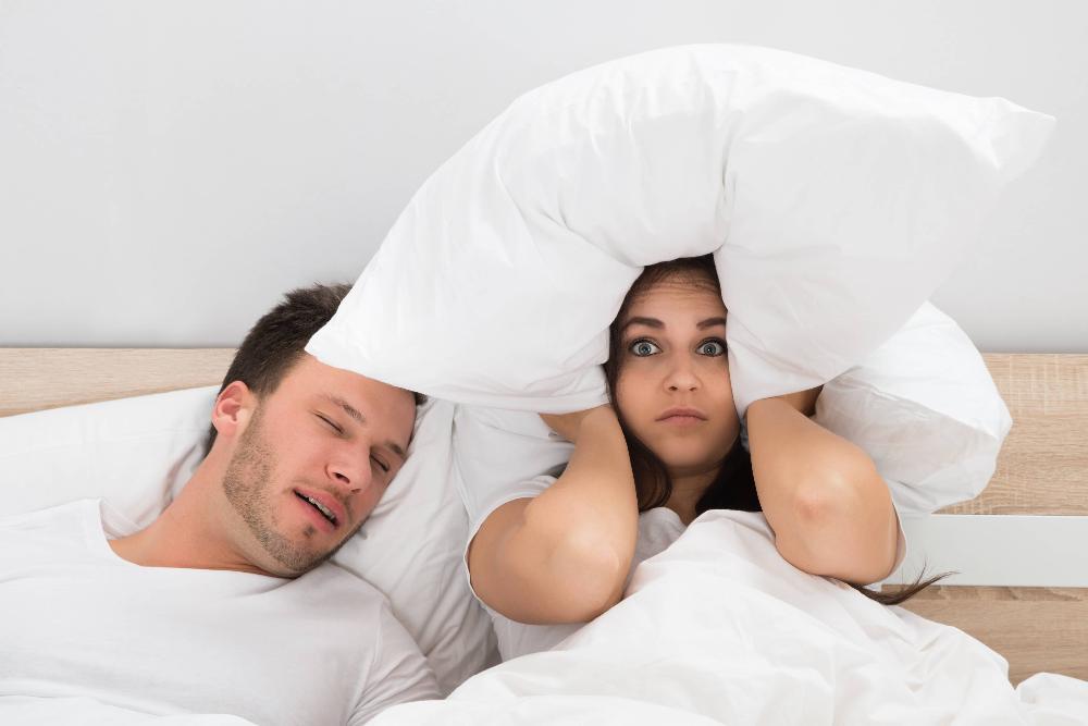 woman covering ears with pillow while her husband snores