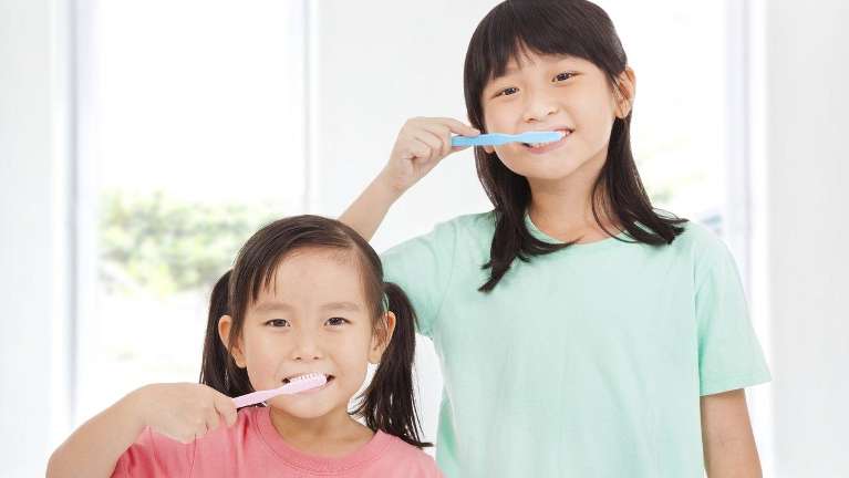 two young girls brushing their teeth