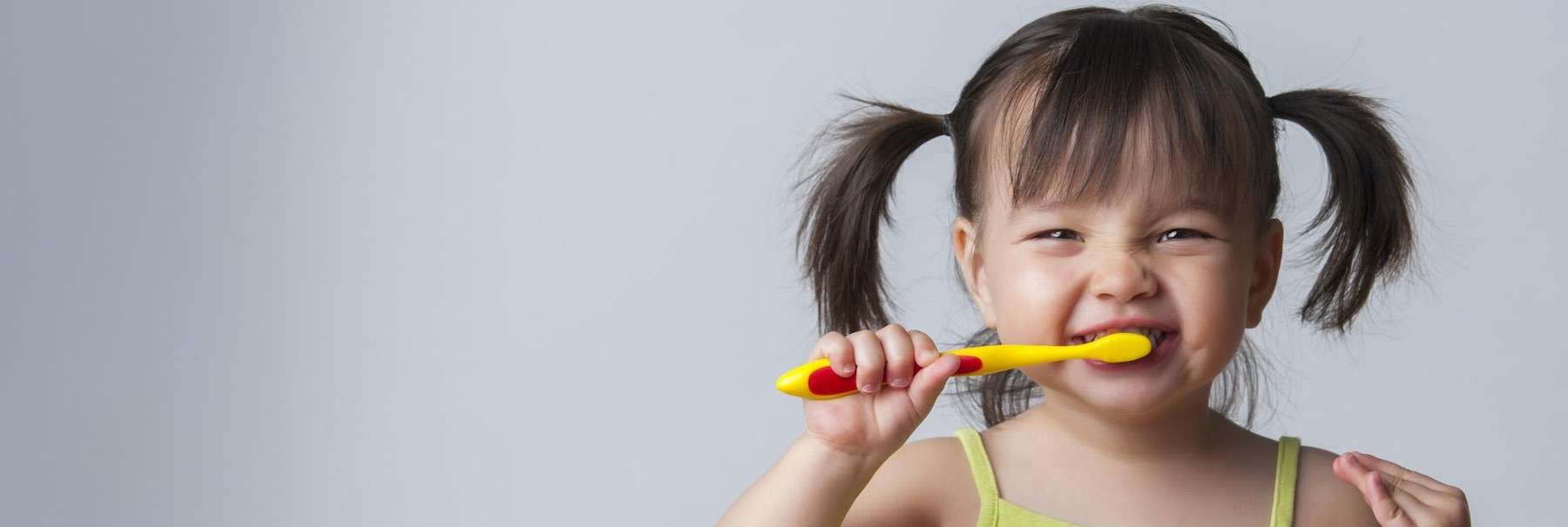 Young girl with pigtails brushing her teeth with a yellow toothbrush.