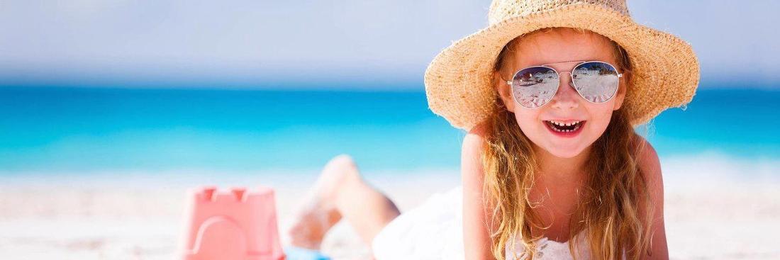 youn girl sitting on beach with sunglasses and sun hat