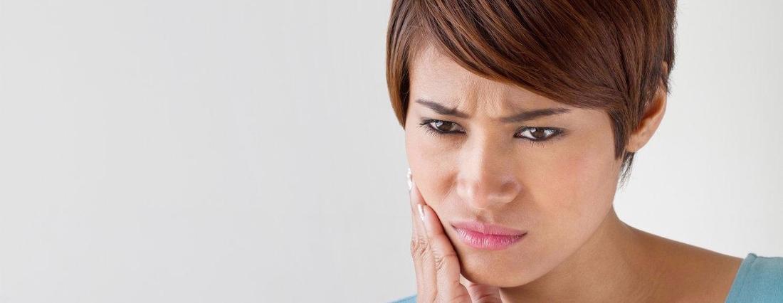 a woman holds her hand to her mouth from pain during a dental emergency